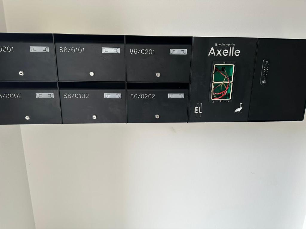 apartment 1 Zwarte modulaire wandbrievenbus met vier postvakken en codepaneel, gemonteerd op een bakstenen muur.